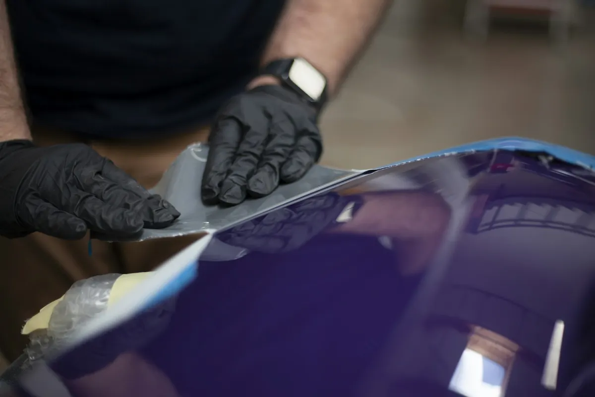 Operatore con guanti che applica pellicola su carrozzeria blu